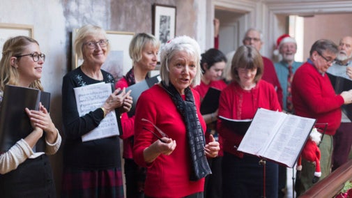 A group of people many in red jumpers standing in a hallway singing